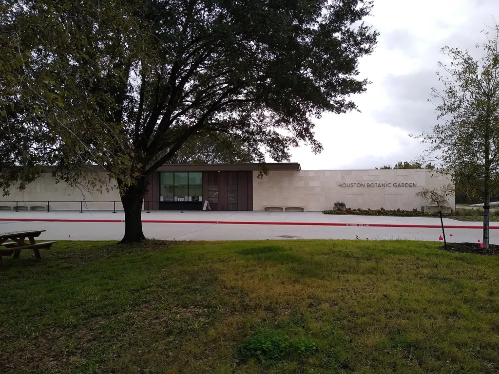 The low pale entrance building of the Houston Botanic Garden behind a lawn and a broad oak tree